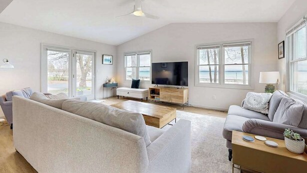 Un salón amplio con un sofá grande, una mesa de centro y una televisión. Grandes ventanas ofrecen vistas al exterior.