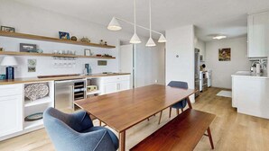 Una cocina moderna con armarios blancos, una mesa de comedor de madera e iluminación colgante.