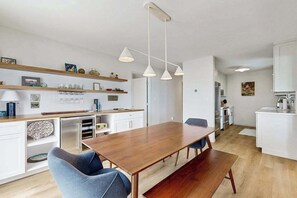 A modern kitchen with white cabinetry, a wooden dining table, and pendant lighting. - Tranquil Lakeview Retreat in Suttons Bay, with a private sauna, & large yard (Suttons Bay)