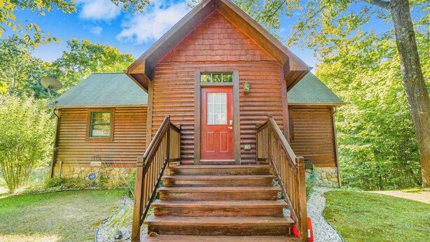 Une cabane en rondins avec une porte rouge, un revêtement extérieur en bois et un escalier menant à l’entrée.