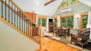 Une pièce spacieuse avec un escalier en bois, de grandes fenêtres, un coin repas et une cheminée.