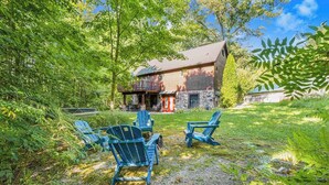 Un chalet rustique avec des fondations en pierre, une véranda avec des chaises et un environnement verdoyant luxuriant.