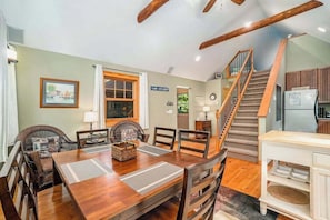 A dining area with a wooden table and chairs, a staircase, and a kitchen area with cabinets.