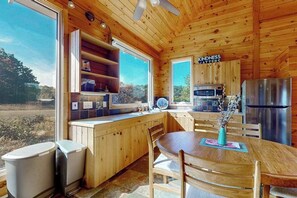 Interior de una cabaña de madera con cocina, comedor y ventanas grandes.