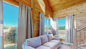 En stuga byggd av trä med en soffa, stora fönster och en trappa av trä.