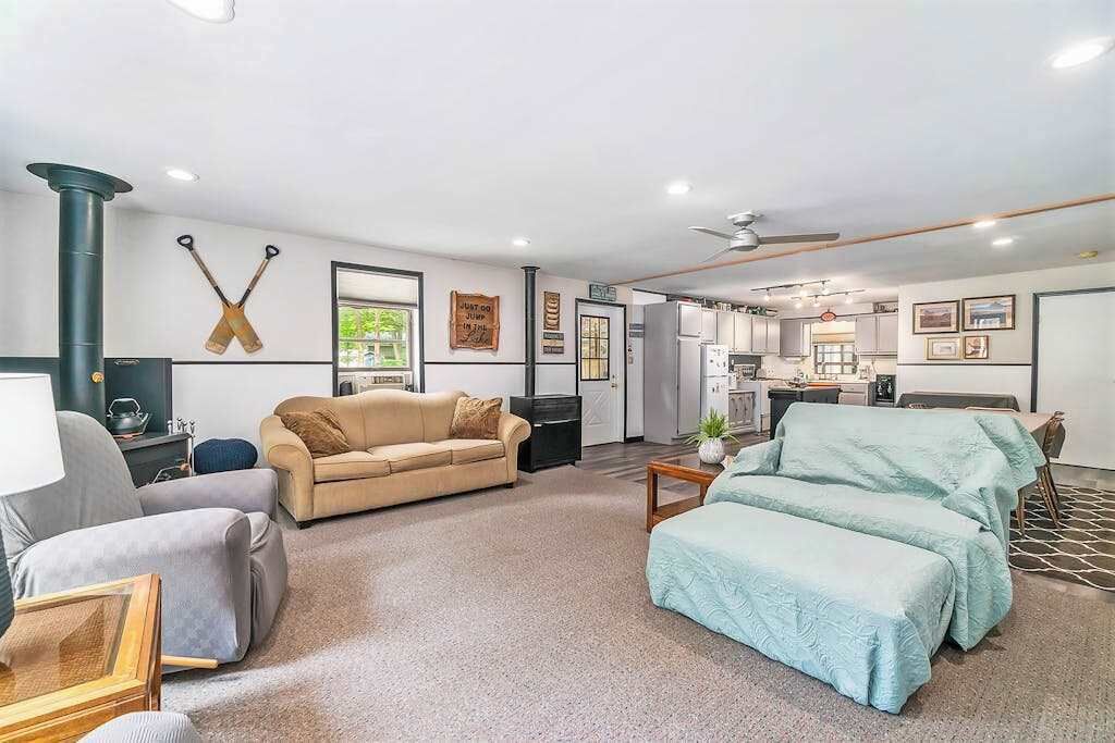 A modern living room with a sofa, a coffee table, and a TV. There is a kitchen area with cabinets and a refrigerator.