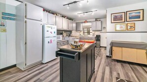 A modern kitchen with white cabinets, a central island, and a dining area with a bench. - Cardinal Cabin | House in Honor (Honor)