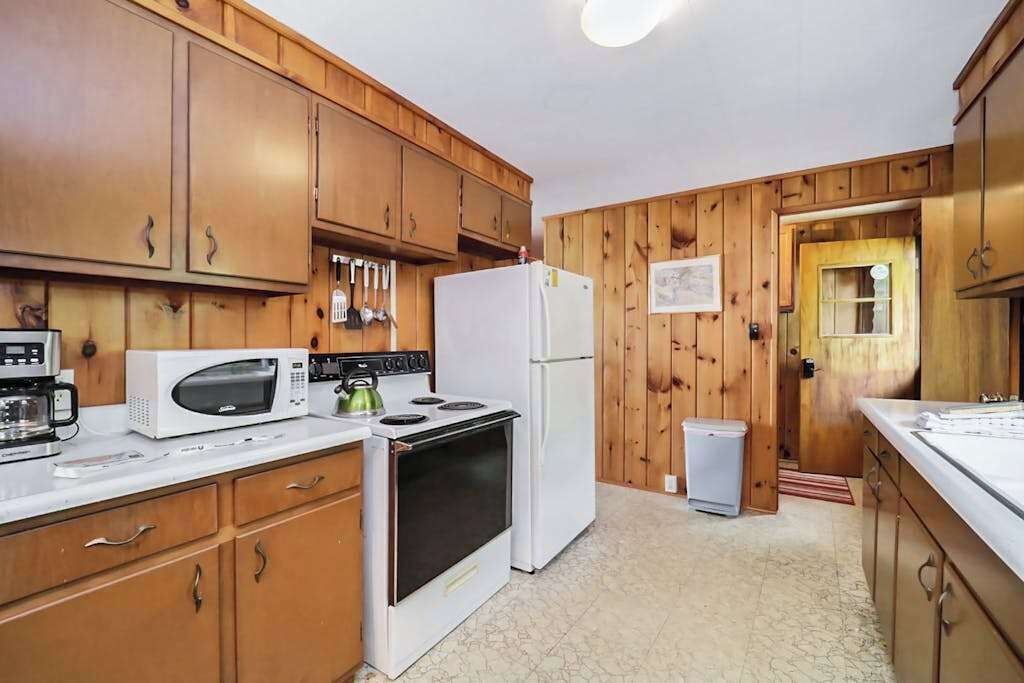 A kitchen with wooden cabinets, a microwave, stove, refrigerator, and a trash bin.
