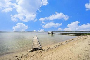 A clear sky, a sandy beach, and a wooden pier leading to a dock.