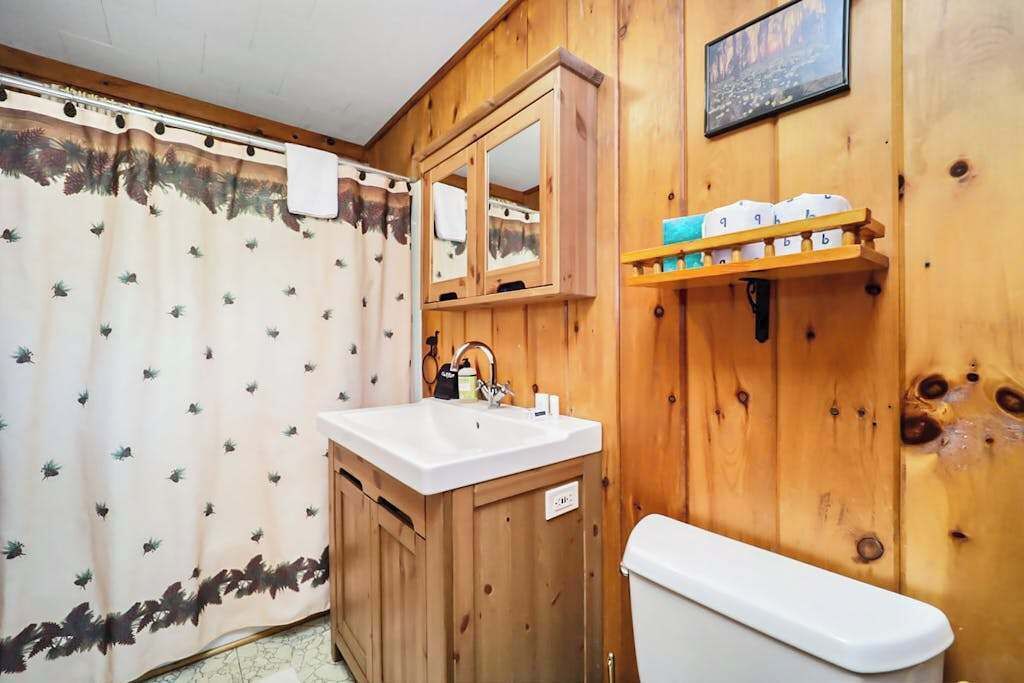 A wooden bathroom with a shower curtain, a sink, a mirror, and a toilet.