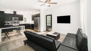 A modern kitchen with dark cabinets, a microwave, and a refrigerator. There is a black sofa and a coffee table in the living area. - Secluded & contemporary cottage with a washer/dryer, central AC, & firepit (Honor)
