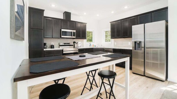 A modern kitchen with dark cabinets, stainless steel appliances, and a central island with stools. - Secluded & contemporary cottage with a washer/dryer, central AC, & firepit (Honor)
