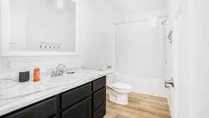 A modern bathroom with a white sink, dark cabinets, a large mirror, and a shower area. - Secluded & contemporary cottage with a washer/dryer, central AC, & firepit (Honor)