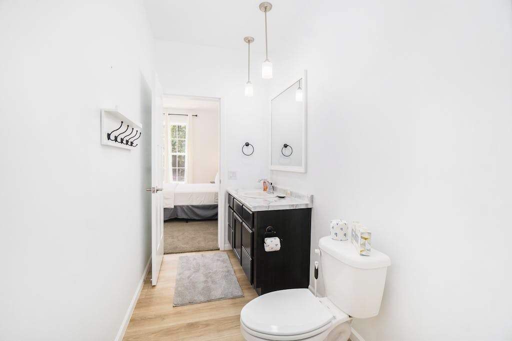 Un bagno moderno con WC, lavandino e specchio. Sul pavimento è presente un piccolo tappeto e una porta che conduce in un'altra stanza.