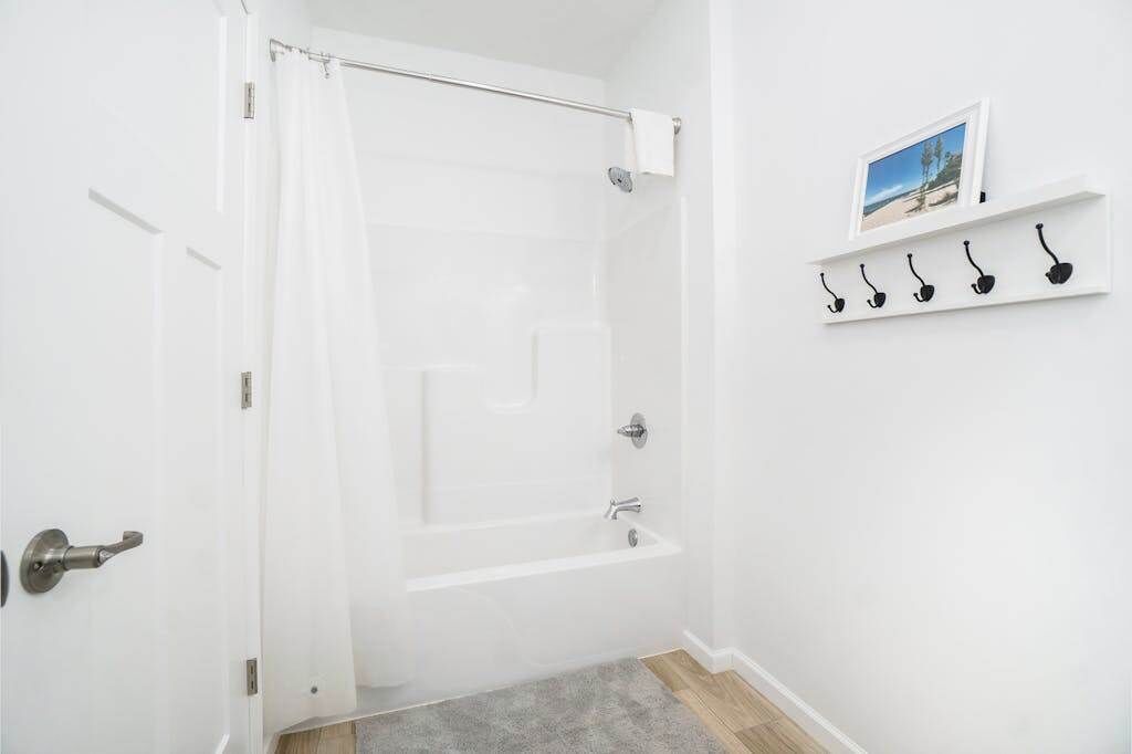 A bathroom with a bathtub, a shower curtain, a towel rack with hooks, and a framed picture on the wall.