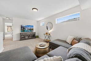A spacious living room with a gray sofa, a round coffee table, and a painting on the wall. - Old Town North Retreat | Bikes, Brews & Trails (Fort Collins)