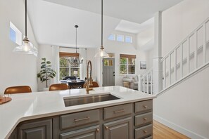 A spacious kitchen with a central island, pendant lighting, and a staircase leading to an upper level. - Old Town North Retreat | Bikes, Brews & Trails (Fort Collins)
