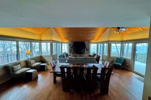A spacious room with a wooden ceiling, a fireplace, a dining table with chairs, and large windows offering a view. - Secluded lake-view home with large deck, private gas grill, AC (Harbor Springs)