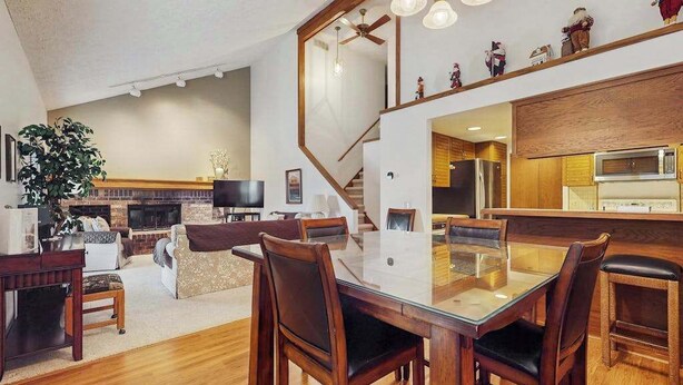A modern living room with a glass dining table, wooden chairs, a fireplace, and a kitchen area with a microwave. - Spacious 3-level retreat w/ fireplace, wet bar, deck, tennis, skiing & golf near (Harbor Springs)
