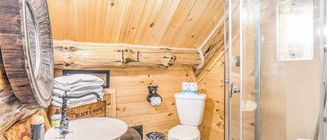 Un baño de cabaña de madera con lavamanos, inodoro y ducha.