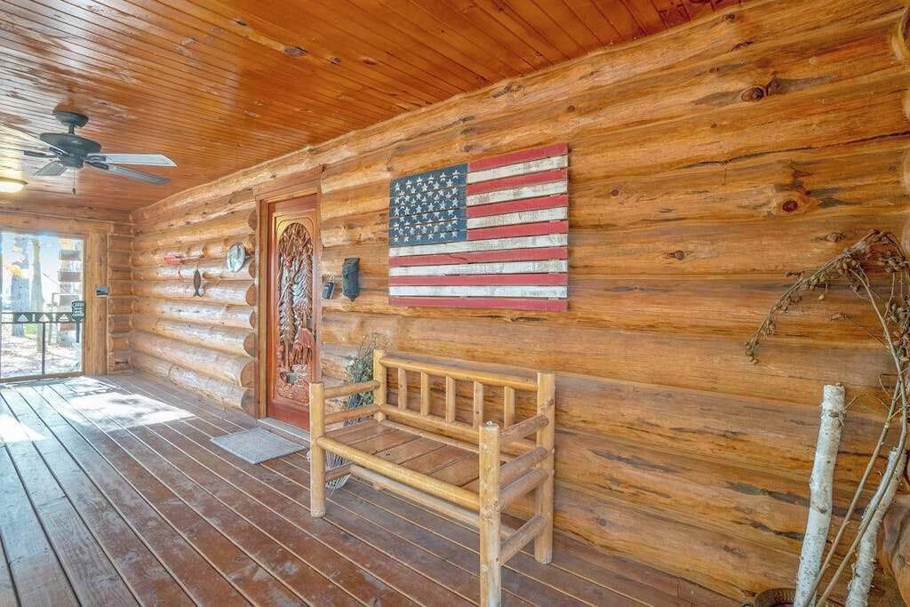 Une cabane en rondins avec un banc en bois, un ventilateur de plafond et un drapeau américain accroché au mur.