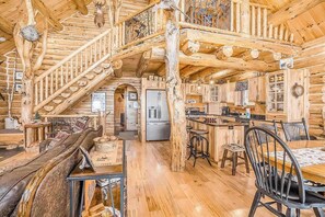 A log cabin interior with a wooden staircase, a dining area, and a kitchen. - Delightful Riverfront Cabin with Wood-Burning Fireplace and Gas Grill & Hot Tub (Thompsonville)
