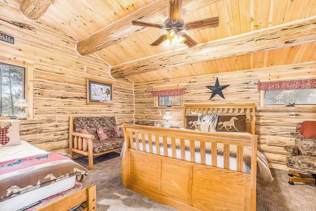 A log cabin interior with a crib, a rocking chair, and a bed.