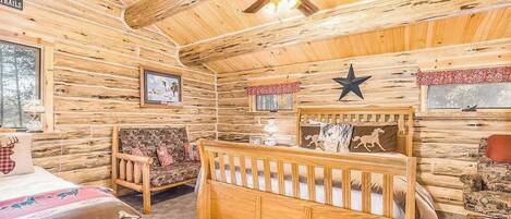 A log cabin interior with a crib, a rocking chair, and a bed.