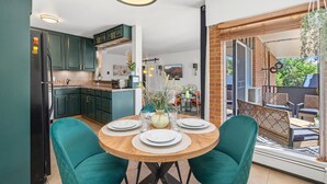 A modern kitchen with teal cabinets, a dining area with a round table, and a view of the outdoors. - The Aviary Near CSU | Pool, Sauna, and Gym (Fort Collins)