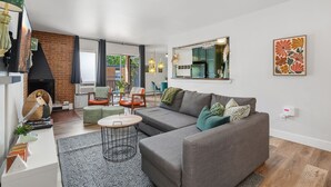 A modern living room with a sofa, a coffee table, a fireplace, and a dining area with chairs. - The Aviary Near CSU | Pool, Sauna, and Gym (Fort Collins)