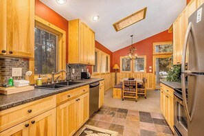 A kitchen with wooden cabinets, a sink, a stove, and a dining area with a table and chairs. - Family-friendly rustic cabin next to the slopes of Crystal Mountain (Thompsonville)