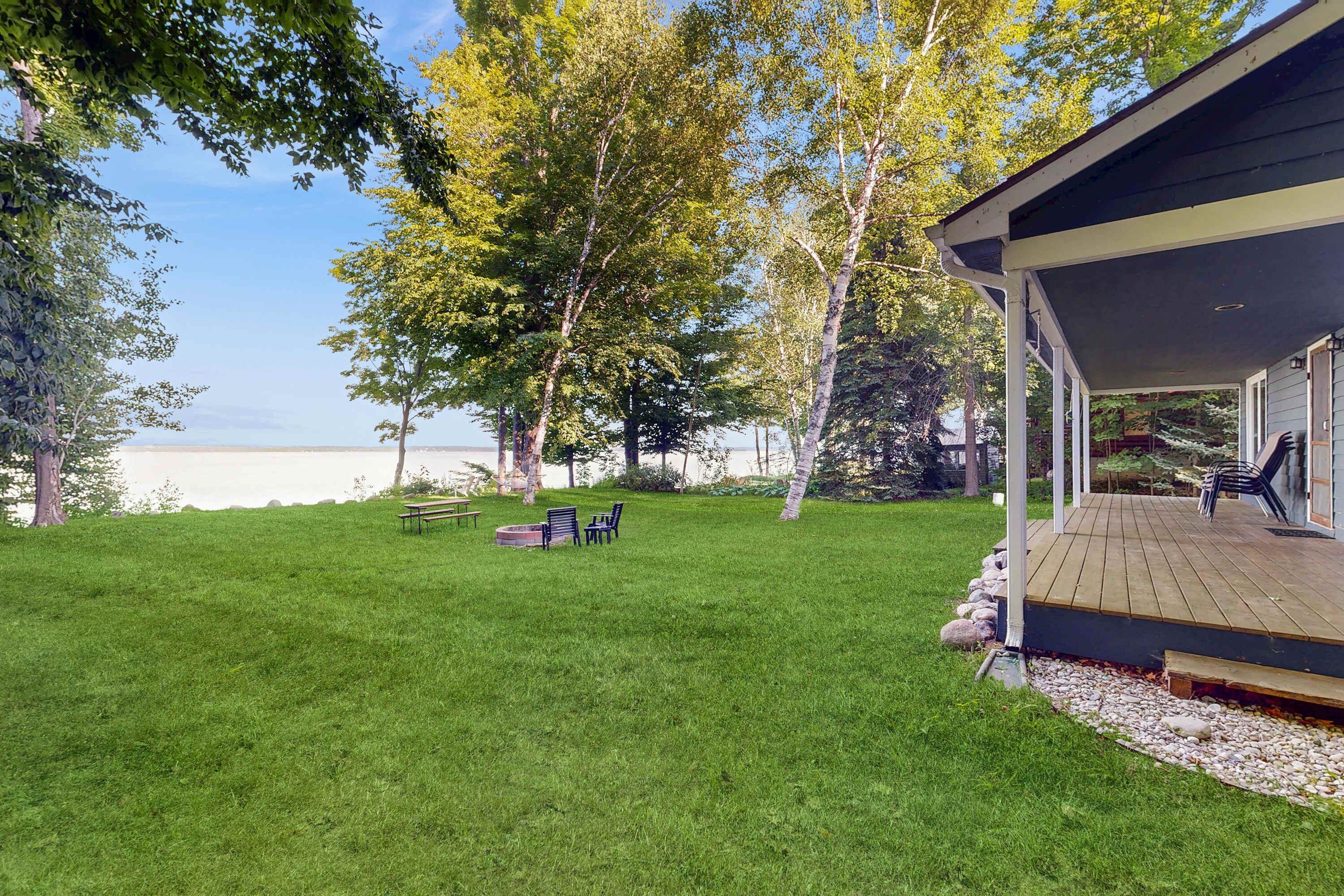 A grassy backyard with a wooden deck, outdoor seating, and a view of a body of water.