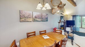 Una zona de menjador amb taula i cadires de fusta, un penjallum i obra d'art penjada a la paret.