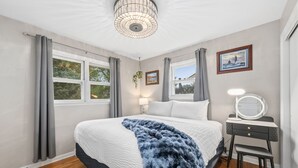 A bedroom with a bed, a desk with a mirror, and a window with curtains. - Sandstone Hollow | King Suite, Office, Fenced Yard (Fort Collins)