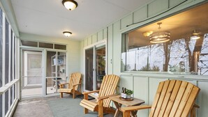 A covered porch with wooden chairs and a table, large windows, and a ceiling light fixture. - Sandstone Hollow | King Suite, Office, Fenced Yard (Fort Collins)