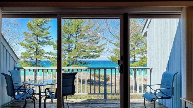 A balcony with a table and chairs, a view of the sea, and trees. - Waterfront condo near skiing with beach access, on-site golf & fireplace (Glen Arbor)