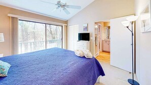 A bedroom with a bed, a ceiling fan, a TV, and a view of the outdoors. - Waterfront condo near skiing with beach access, on-site golf & fireplace (Glen Arbor)