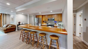 A modern kitchen with wooden cabinets, a stainless steel refrigerator, a microwave, and a stand mixer. There are four wooden stools at the bar counter. - Stylish retreat with a full kitchen, sunroom, & W/D access (Glen Arbor)