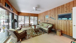 A room with a wooden interior, a ceiling fan, a sofa, a table, and a window with a view of trees. - Two-story home with a patio, sunroom, balcony, & washer/dryer access (Glen Arbor)