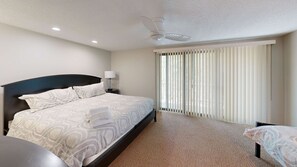 A hotel room with a bed, a nightstand, a lamp, a ceiling fan, and a large window with blinds. - Two-story home with a patio, sunroom, balcony, & washer/dryer access (Glen Arbor)