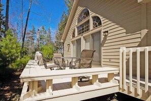 A wooden deck with a table and chairs, a covered seating area, and a window with a view of trees. - Dog-friendly home near the lake with a deck, fireplace, washer/dryer (Glen Arbor)