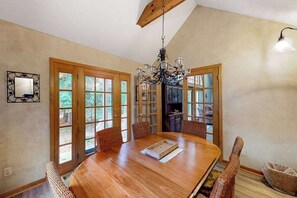 A dining room with a wooden table, wicker chairs, a chandelier, and a view through French doors. - Dog-friendly home near the lake with a deck, fireplace, washer/dryer (Glen Arbor)