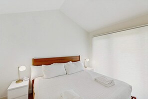 Ein ordentlich bezogenes Bett mit Holz-Kopfteil, weißer Bettwäsche und einem gefalteten Handtuch an der Seite.