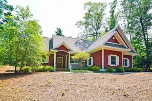 A two-story house with a front porch, a red exterior, and a well-maintained yard. - Downtown home near the lake with washer/dryer, firepit, backyard (Glen Arbor)