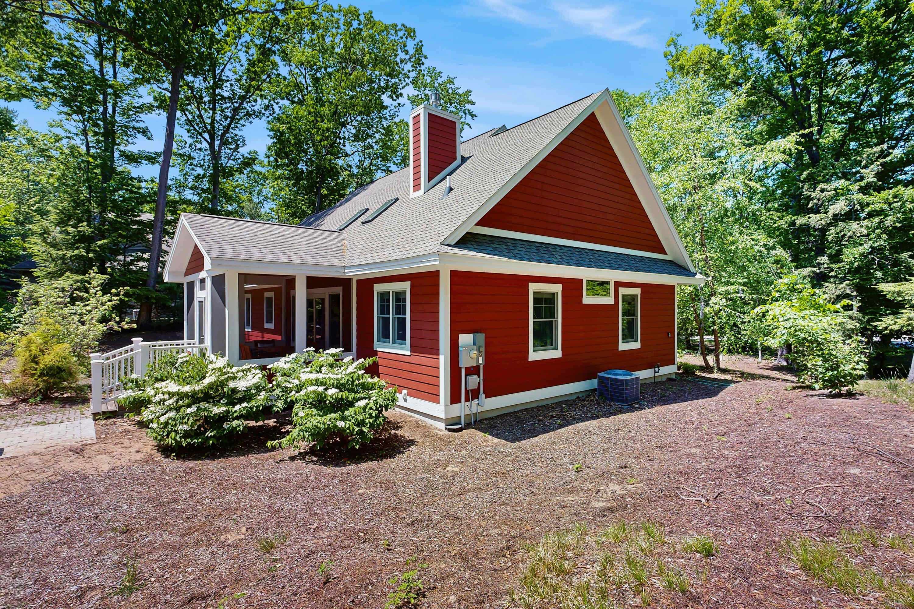 A red house with a white porch, a chimney, and a gravel driveway.