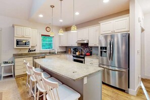 A modern kitchen with white cabinets, stainless steel appliances, and a central island with bar stools. - Downtown home near the lake with washer/dryer, firepit, backyard (Glen Arbor)