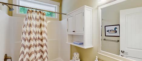A bathroom with a shower curtain, toilet, sink, and a framed picture on the wall.