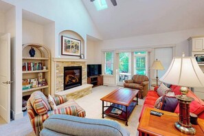 A living room with a fireplace, a television, a sofa, a coffee table, and a lamp. - Downtown home near the lake with washer/dryer, firepit, backyard (Glen Arbor)