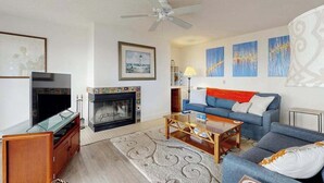 Ein Wohnzimmer mit Fernseher, Kamin, Sofa, Couchtisch und Deckenventilator.