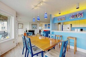 Un coin repas avec une table en bois et des chaises bleues, une cuisine avec des meubles bleus et des œuvres d’art accrochées aux murs.